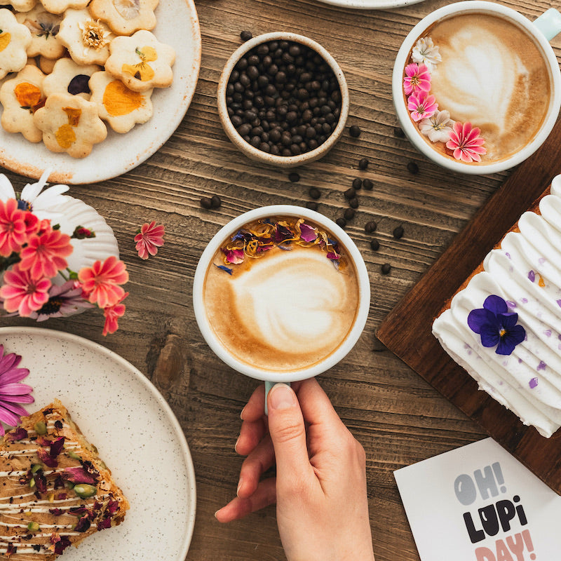 Un café de lupin avec de la mousse de lait entouré de nombreuses pâtisseries et une carte de la marque Lupi Coffee