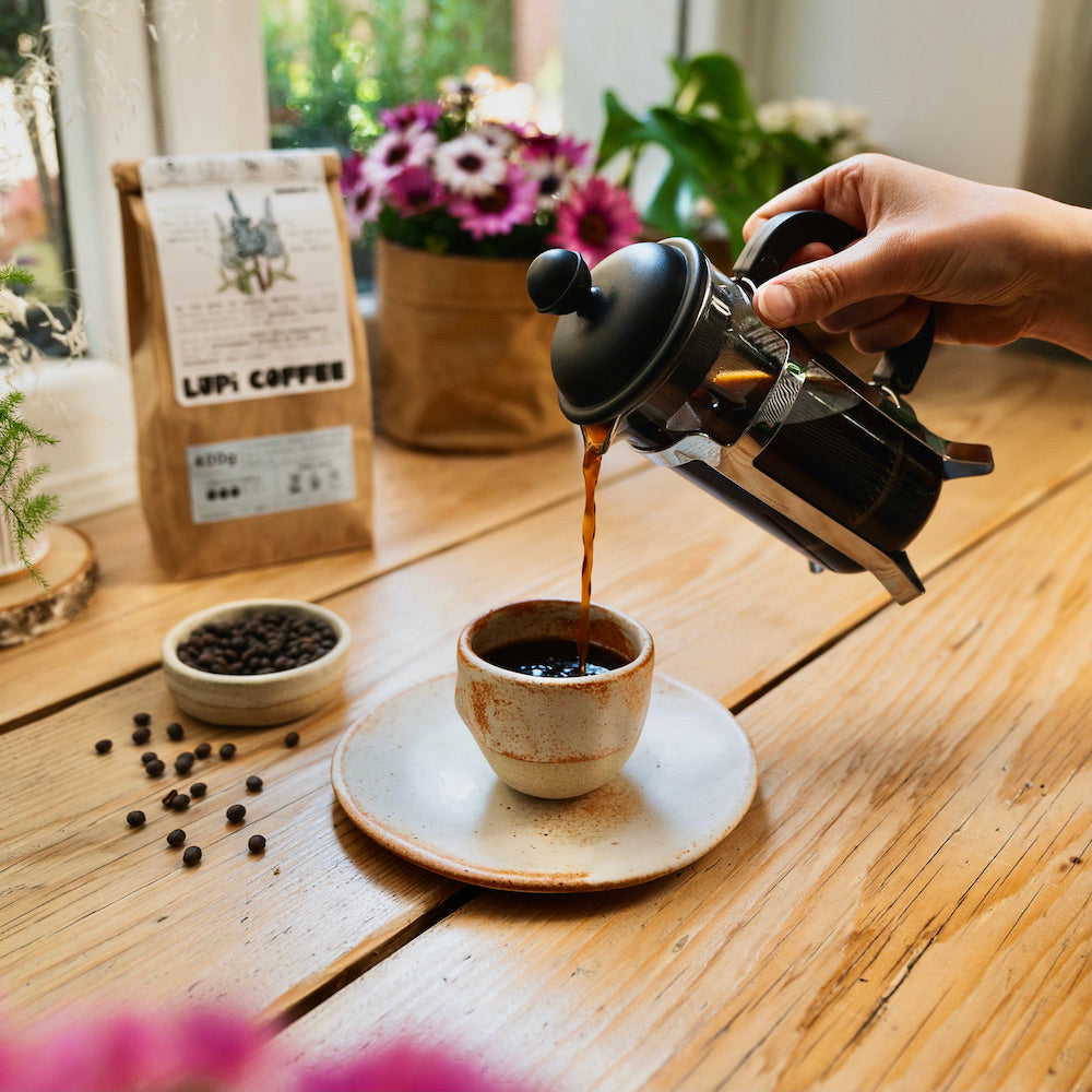 Une main qui verse du café de lupin de la marque Lupi Coffee d'une cafetière à piston dans une tasse de Albane Trollé